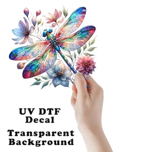 May include: A colorful stained glass dragonfly with blue, green, red, and yellow accents is surrounded by pink, purple, and white flowers. The text "UV DTF Decal Transparent Background" is below the image.