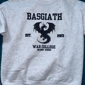 May include: A gray sweatshirt with a black dragon graphic and the text "BASGIATH EST. 2023 WAR COLLEGE DRAGON RIDERS"