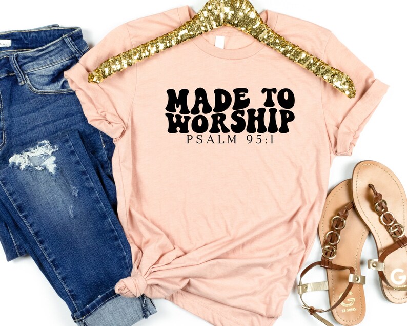 May include: A light pink t-shirt with black text that reads "Made to Worship Psalm 95:1". The text is in a retro font style.