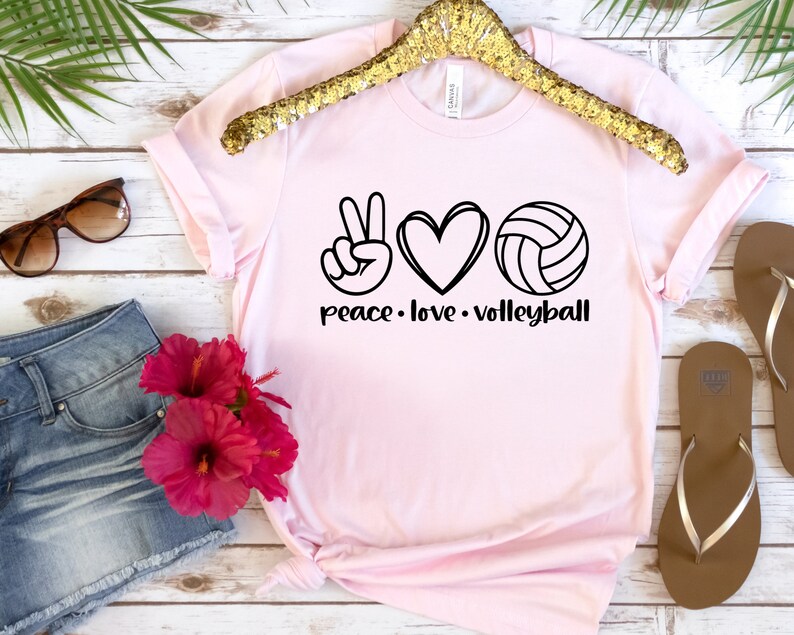 K&ouml;nnte beinhalten: Rosa T-Shirt mit einem Peace-Zeichen, einem Herzen und einem Volleyball-Motiv. Der Text "peace. love. volleyball" ist unter dem Motiv gedruckt.