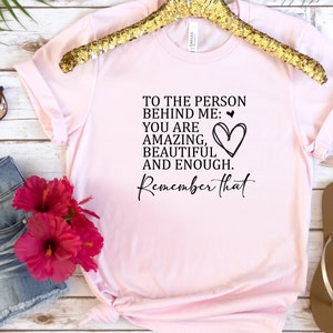 May include: Pink t-shirt with a black graphic that reads "To the person behind me: You are amazing, beautiful and enough. Remember that." with a heart drawn next to the text.
