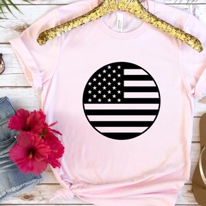 May include: A pink t-shirt featuring a black and white circular design of the American flag.