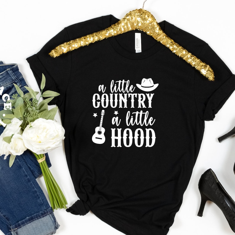 May include: A black t-shirt with a white graphic that says "a little country a little hood" with a cowboy hat, guitar, and stars.