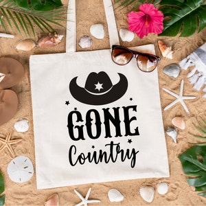 May include: White canvas tote bag with black text and a black silhouette of a cowboy hat. The text reads "Gone Country".