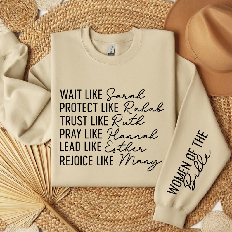 May include: A beige sweatshirt with black text that reads "WAIT LIKE Sarah PROTECT LIKE Rahah TRUST LIKE Ruth PRAY LIKE Hannah LEAD LIKE Esther REJOICE LIKE Many" on the front and "WOMEN OF THE Bible" on the sleeve.