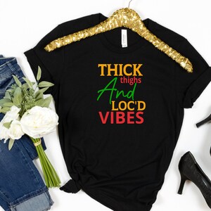 May include: Black t-shirt with the text "THICK thighs And LOC'D VIBES" in green, red, and yellow lettering.