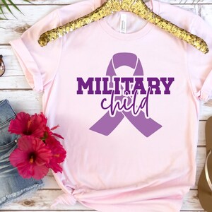 May include: A pink t-shirt with a purple ribbon and the text "MILITARY child" in purple lettering.