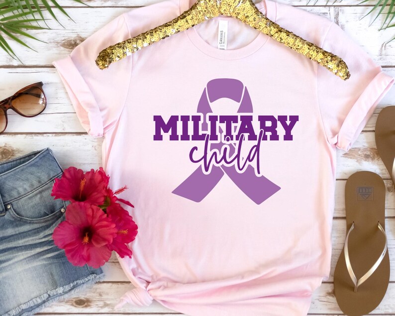 May include: A pink t-shirt with a purple ribbon and the text "MILITARY child" in purple lettering.