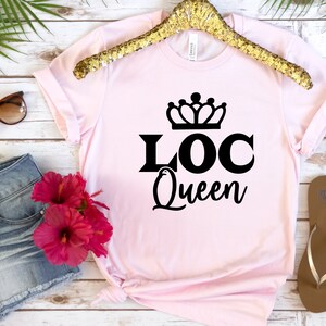 May include: Pink t-shirt with a black crown and the text "LOC Queen" printed on the front.