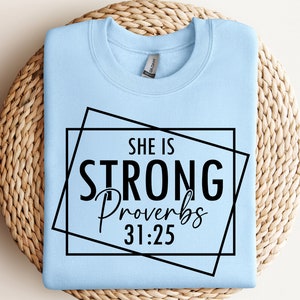 May include: Light blue sweatshirt with a black graphic that says "She is Strong Proverbs 31:25" inside two black square frames.