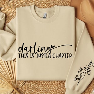 May include: A beige sweatshirt with the text "darling this is just a chapter" on the front and "not the whole story" on the sleeve.