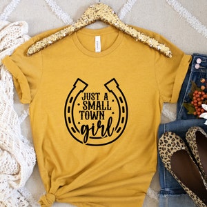 May include: A mustard yellow t-shirt with a black horseshoe graphic and the text "Just a Small Town Girl".