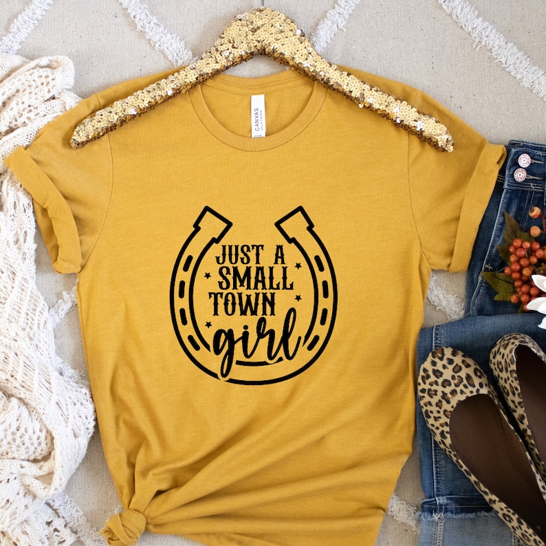 May include: A mustard yellow t-shirt with a black horseshoe graphic and the text "Just a Small Town Girl".