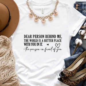 May include: White t-shirt with a black text graphic that reads "Dear person behind me, the world is a better place with you in it. -the person in front of you".