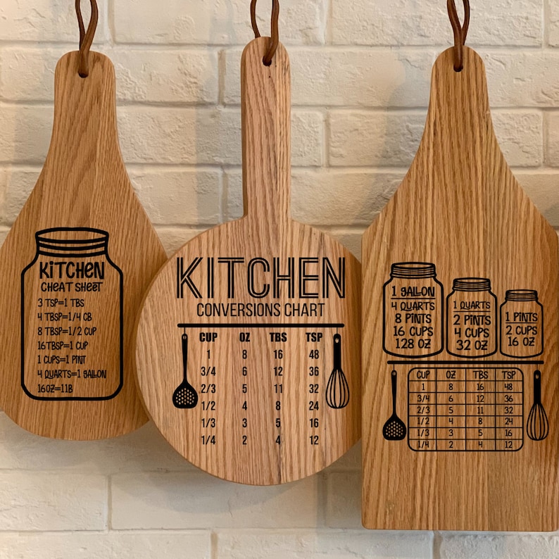 May include: Three wooden cutting boards with kitchen conversion charts and cheat sheets. The boards are made of light brown wood and have black text and graphics. The first board has a cheat sheet with conversions for teaspoons, tablespoons, cups, pints, quarts, and gallons. The second board has a conversion chart for cups, ounces, tablespoons, and teaspoons. The third board has a conversion chart for gallons, quarts, pints, and cups.