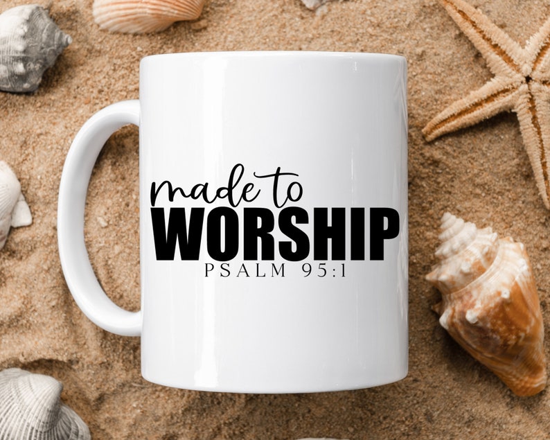 May include: White ceramic mug with black text that reads "made to worship" and "PSALM 95:1". The mug is sitting on a sandy surface with seashells and a starfish.