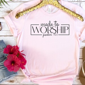 May include: Pink t-shirt with black text that reads "made to WORSHIP psalm 95:1".