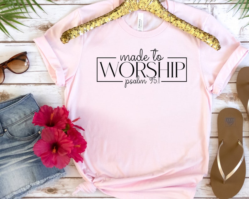 May include: Pink t-shirt with black text that reads "made to WORSHIP psalm 95:1".