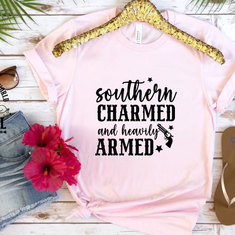 May include: Pink t-shirt with black text that reads "southern CHARMED and heavily ARMED" with a star and a gun graphic.