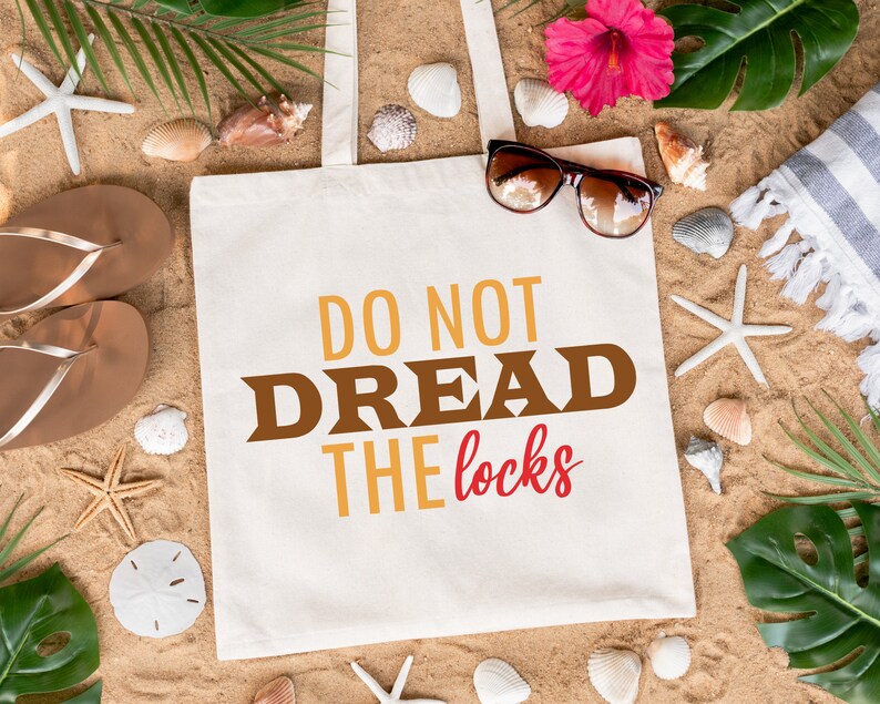 May include: A white tote bag with the text "Do Not Dread The Locks" in brown, yellow, and red letters. The bag is surrounded by seashells, starfish, and tropical plants on a sandy beach.