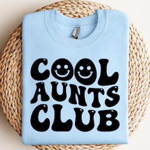 Può includere: Felpa blu chiaro con il testo "Cool Aunts Club" in nero con un font retrò. Il testo include due faccine sorridenti.