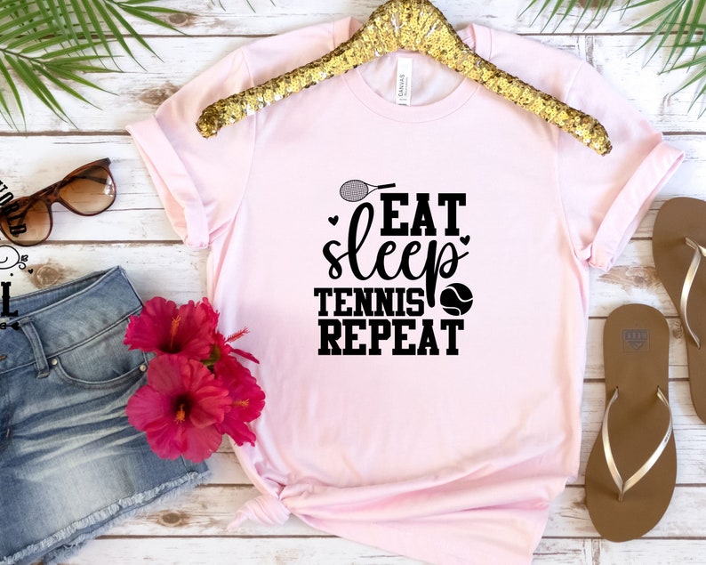 May include: Pink t-shirt with a black graphic that says "Eat Sleep Tennis Repeat" with a tennis racket and tennis ball.
