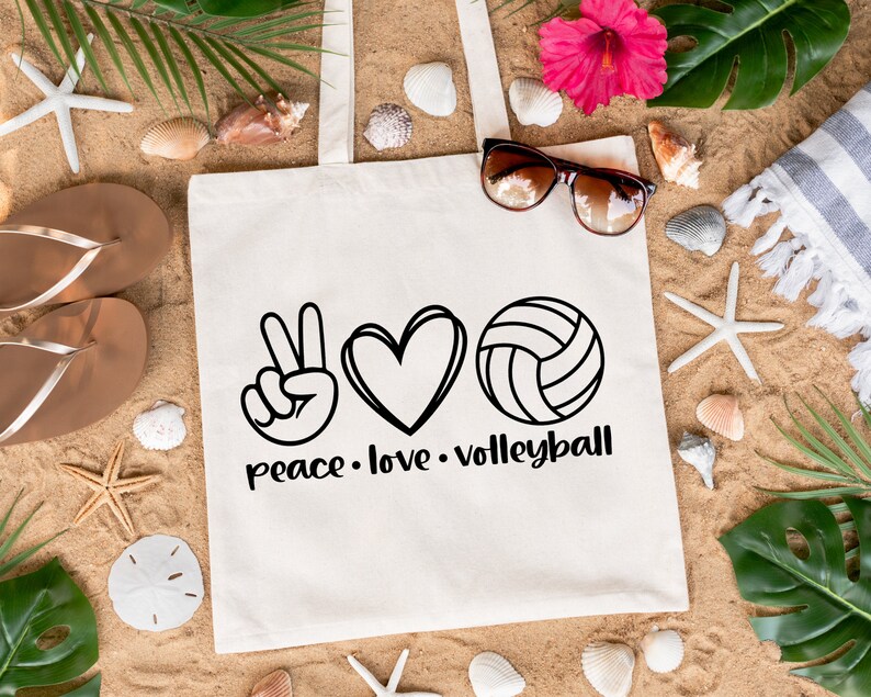 K&ouml;nnte beinhalten: Wei&szlig;e Canvas-Tragetasche mit schwarzem Text, der "peace. love. volleyball" lautet. Die Tasche zeigt ein Peace-Zeichen, ein Herz und eine Volleyball-Grafik.