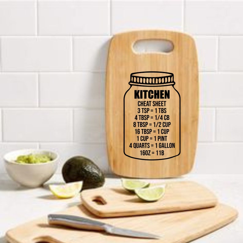 May include: A wooden cutting board with a black and white graphic of a mason jar with the text "Kitchen Cheat Sheet" and a list of kitchen conversions. The conversions include teaspoons, tablespoons, cups, pints, quarts, gallons, and ounces.