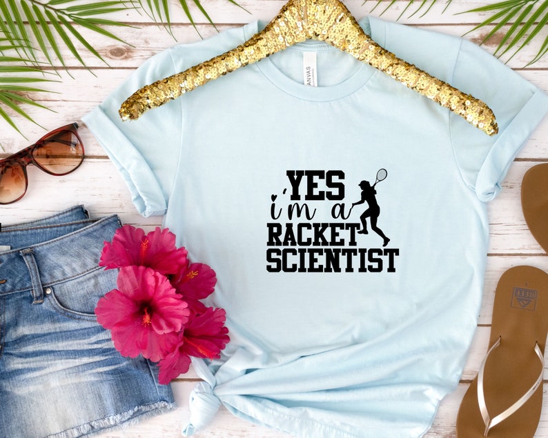 May include: A light blue t-shirt with a black graphic that says "YES i'm a RACKET SCIENTIST" and a silhouette of a person playing tennis.