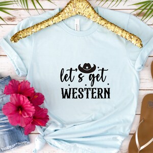 May include: A light blue t-shirt with a black graphic that says "Let's get Western" with a cowboy hat above the text.