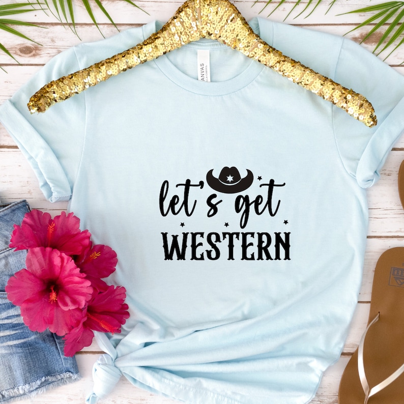 May include: A light blue t-shirt with a black graphic that says "Let's get Western" with a cowboy hat above the text.