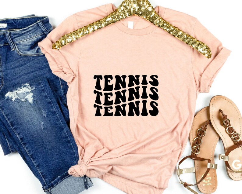 May include: A light pink t-shirt with a black graphic that says "TENNIS" three times in a retro font.