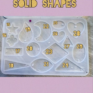 May include: A clear silicone mold with 13 different shapes for resin casting. The shapes include a star, a teardrop, a crescent moon, a heart, a diamond, a rectangle, an oval, a circle, and a triangle. The mold is labeled with numbers 15 through 29.