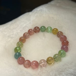 May include: A multi-colored gemstone bracelet with round beads in shades of pink, green, and yellow.