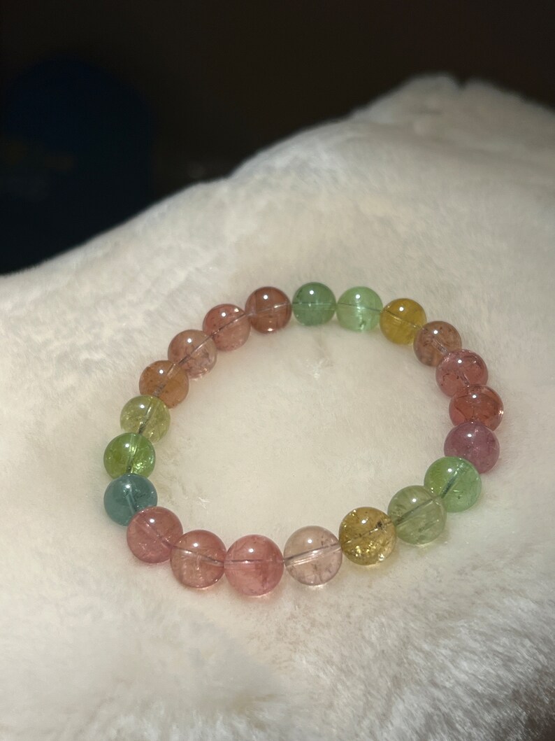 May include: A multi-colored gemstone bracelet with round beads in shades of pink, green, and yellow.
