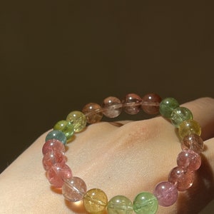 May include: A multi-colored gemstone bracelet with round beads in shades of pink, green, and yellow.