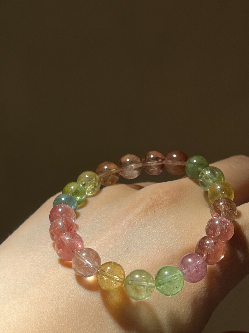 May include: A multi-colored gemstone bracelet with round beads in shades of pink, green, and yellow.