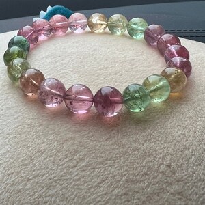 May include: A bracelet made of round, multi-colored gemstones. The bracelet features shades of pink, green, and yellow.