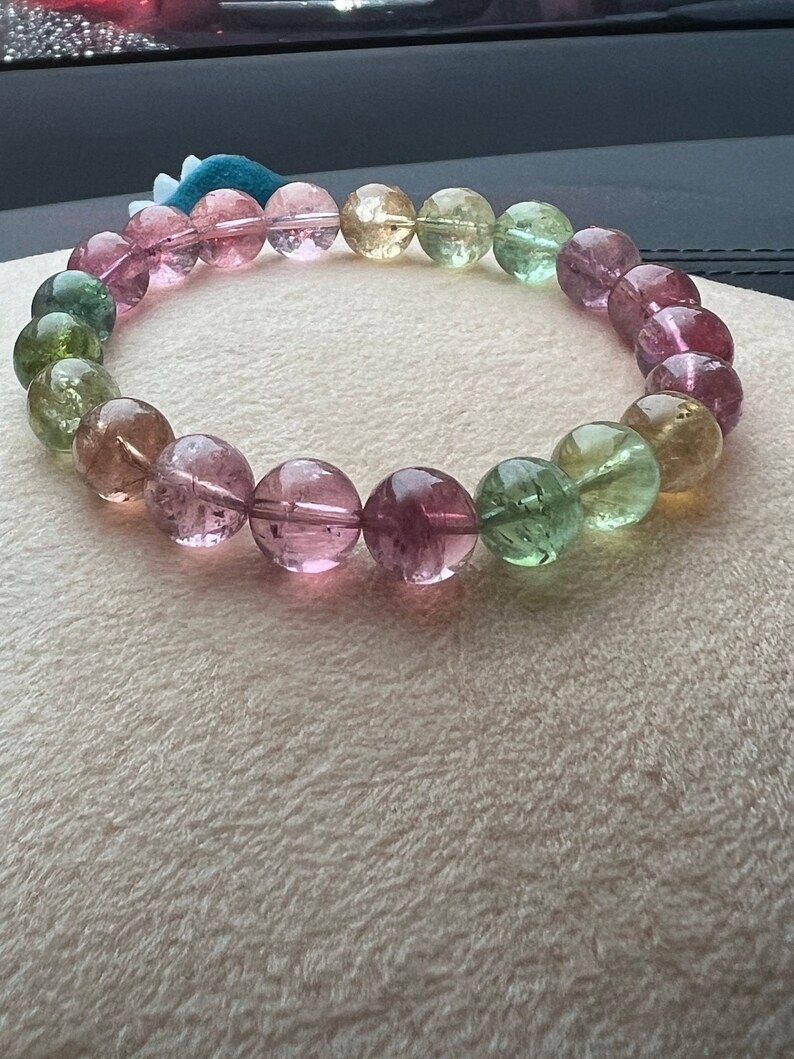 May include: A bracelet made of round, multi-colored gemstones. The bracelet features shades of pink, green, and yellow.