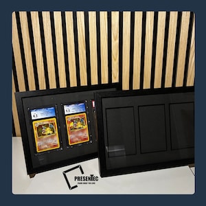 May include: Two black picture frames with glass fronts. The frame on the left has two trading cards inside, one graded 4.5 and the other 9.5. The frame on the right has three empty slots. The frames are on a wood background.