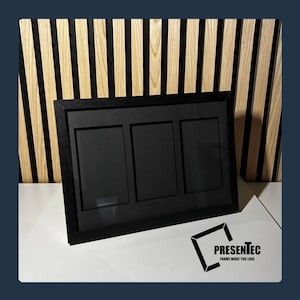 May include: Black triple photo frame with a black mat and a wood grain finish. The frame is on a white surface.