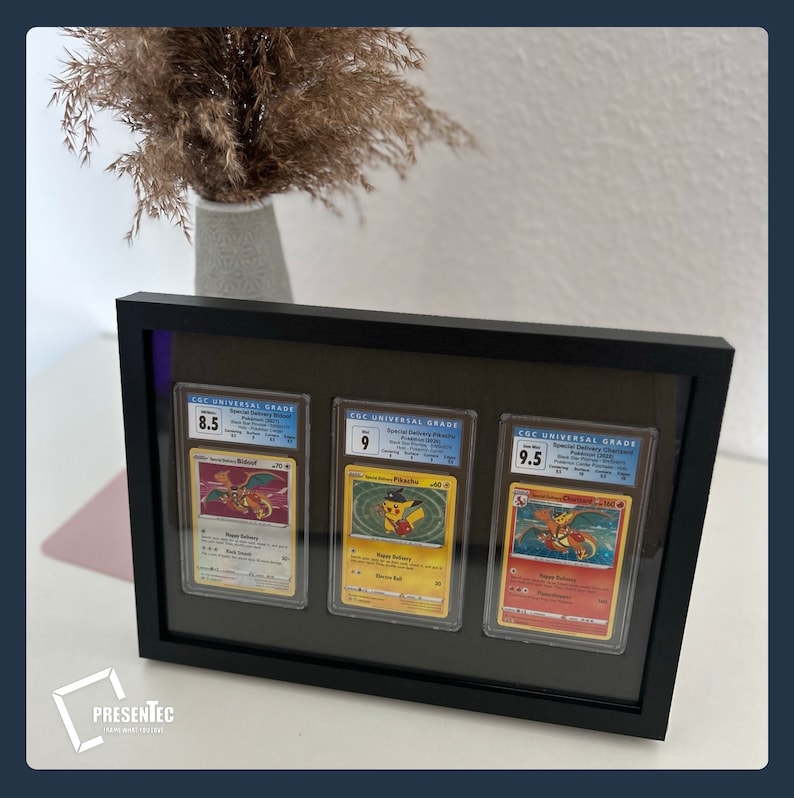 May include: Three Pokemon trading cards are displayed in a black frame. The cards are graded 8.5, 9, and 9.5 by CGC Universal Grade. The cards feature Charizard, Pikachu, and Charizard, respectively.