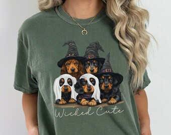 May include: Green t-shirt with a graphic of four dachshund puppies dressed in Halloween costumes. The puppies are wearing witch hats and ghost costumes. The text "Wicked Cute" is printed below the image.
