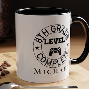 May include: White ceramic mug with a black interior and handle. The mug features a circular design with the text "8th Grade Level Complete" and a game controller graphic. The name "Michael" is printed below the design.