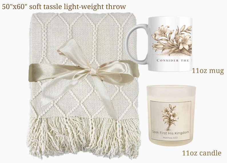 May include: A cream-colored, lightweight throw blanket with a diamond pattern and tassel fringe, tied with a satin ribbon. Includes an 11oz mug and candle, both with floral designs and text that reads "Consider the" and "Seek First His Kingdom".