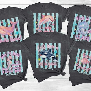 May include: Six charcoal gray t-shirts featuring ocean-themed graphics with light blue vertical stripes, colorful stars, and text including Hello there, This is the -fect CLASS, We're just -ing around, Let's have a of a year, and This is a great year.