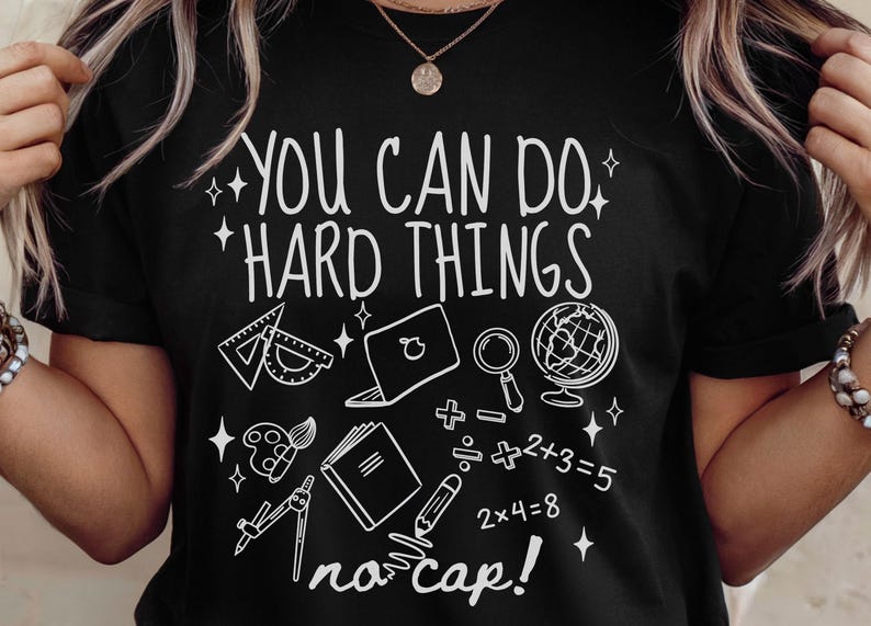 Puede incluir: Camiseta negra con la frase "YOU CAN DO HARD THINGS" en blanco y varios gr&aacute;ficos relacionados con la escuela, incluyendo un transportador, un port&aacute;til, un globo terr&aacute;queo y s&iacute;mbolos matem&aacute;ticos. Tambi&eacute;n incluye la frase "no cap!".