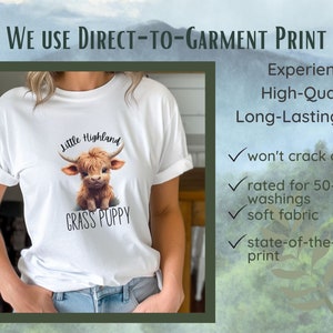 May include: White t-shirt featuring a graphic of a brown and white Highland cow with the text "Little Highland" and "Grass Puppy".