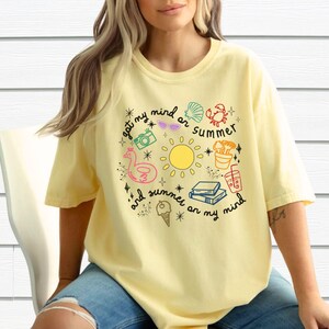 May include: A yellow t-shirt with a graphic design of summer-themed icons and the text "got my mind on summer and summer on my mind".