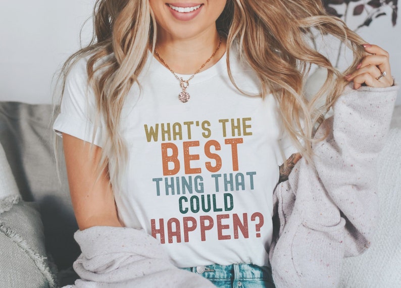 Puede incluir: Camiseta blanca con el texto "What's the best thing that could happen?" en una fuente de estilo vintage con acentos coloridos.
